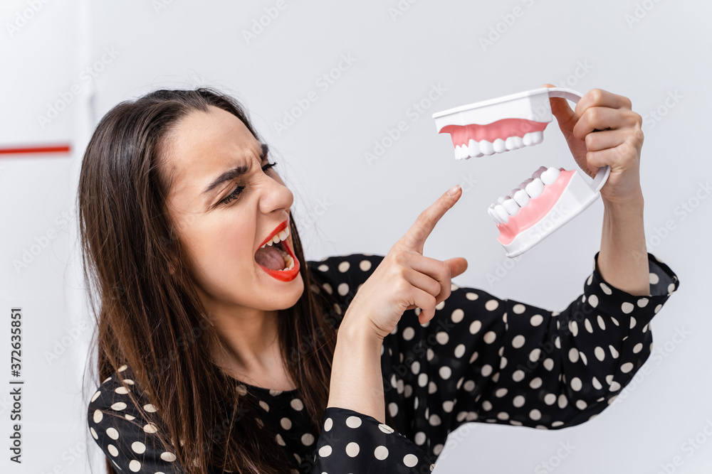 Woman holding educational model of oral cavity with teeth on white background. Funny emotions and ex