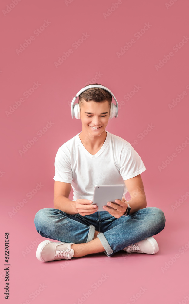 Teenage boy listening to music on color background