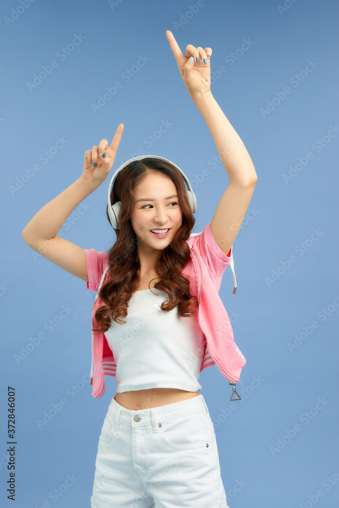 Pretty cool girl having fun and listens to music in the headphones, dancing over blue background.