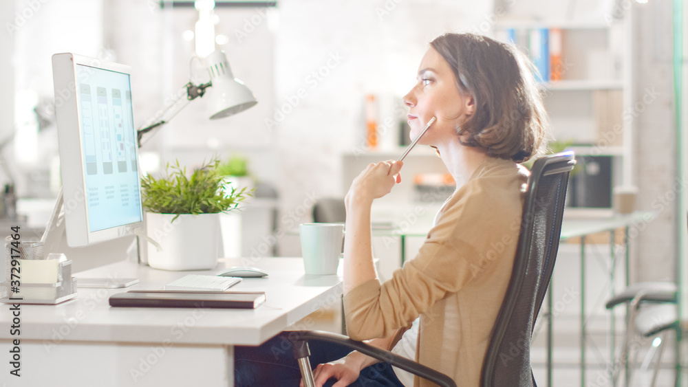 Focused Creative Woman Sitting at Her Desktop Computer in Her Modern Bright Office. She is Thinking 