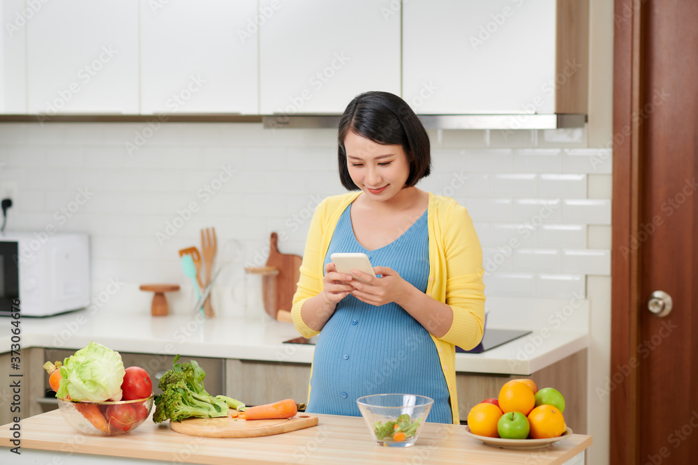 孕妇在厨房准备食物，用手机