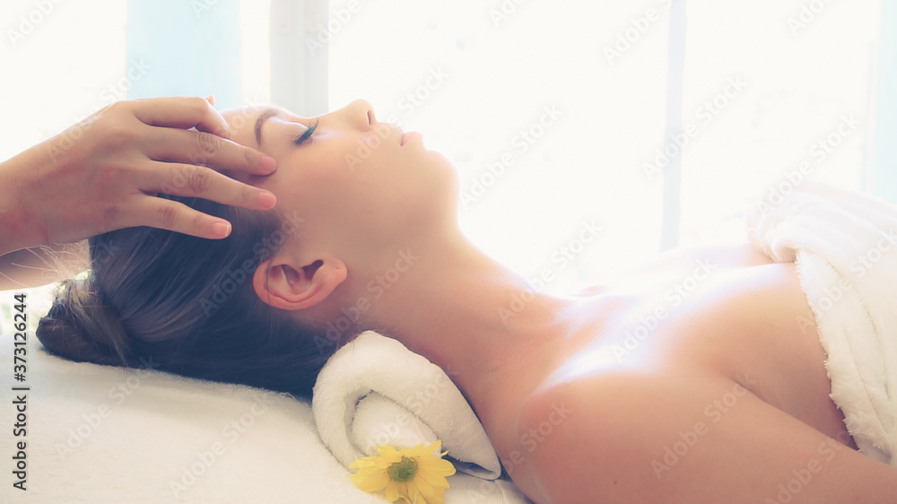 Relaxed woman lying on spa bed for facial and head massage spa treatment by massage therapist in a l