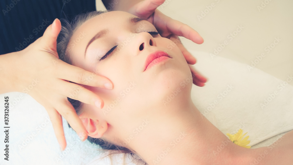 Relaxed woman lying on spa bed for facial and head massage spa treatment by massage therapist in a l