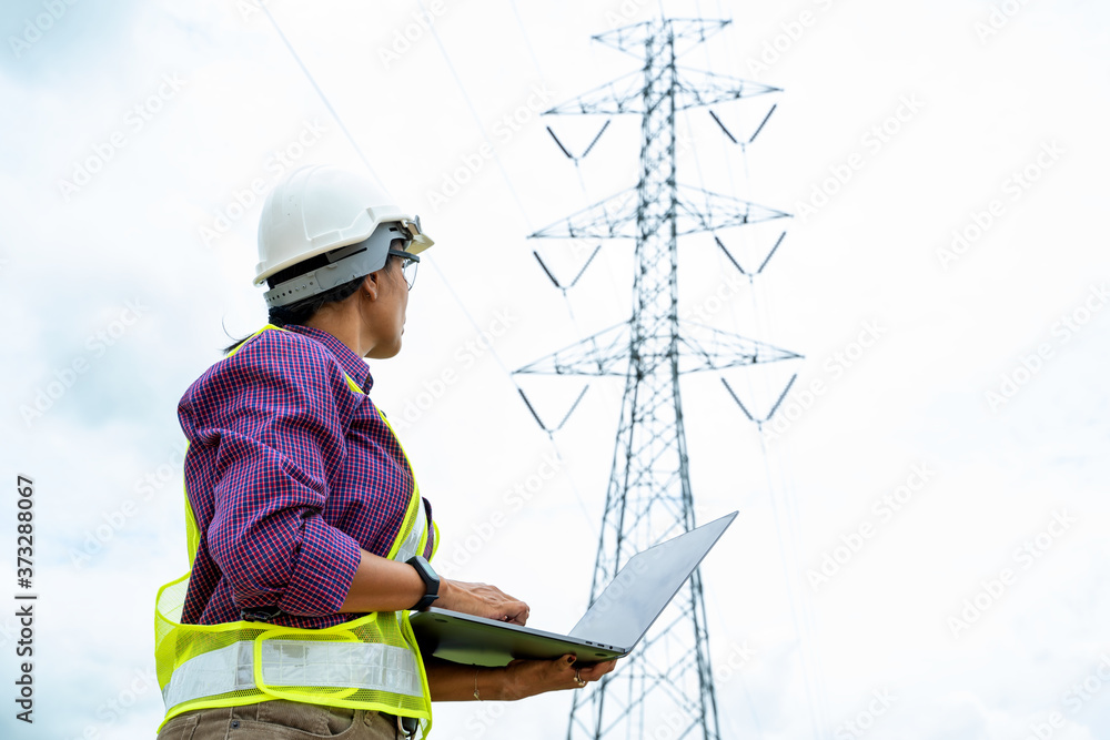 Engineer women using Laptop checking voltage pole Power Transmission.