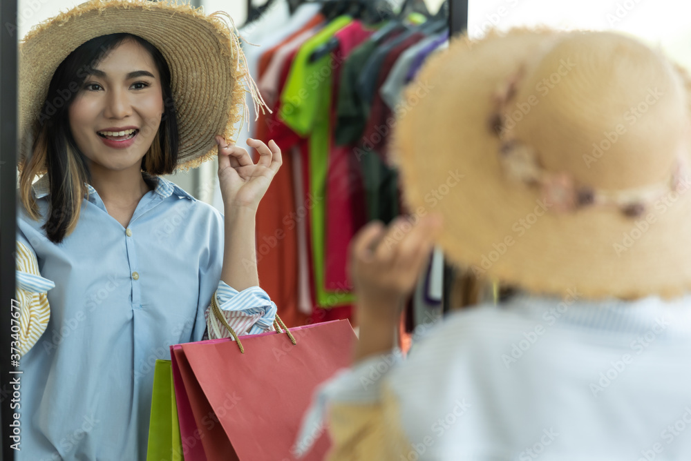 Young woman buying hat and looking in the mirror in the shop.