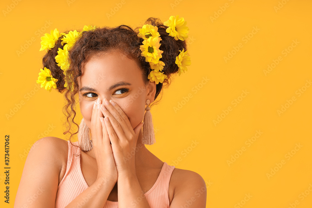 Young African-American woman with beautiful eyeshadows and flowers in her hair on color background