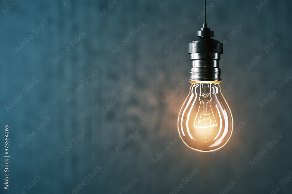 Glowing light bulb on gray wall background.