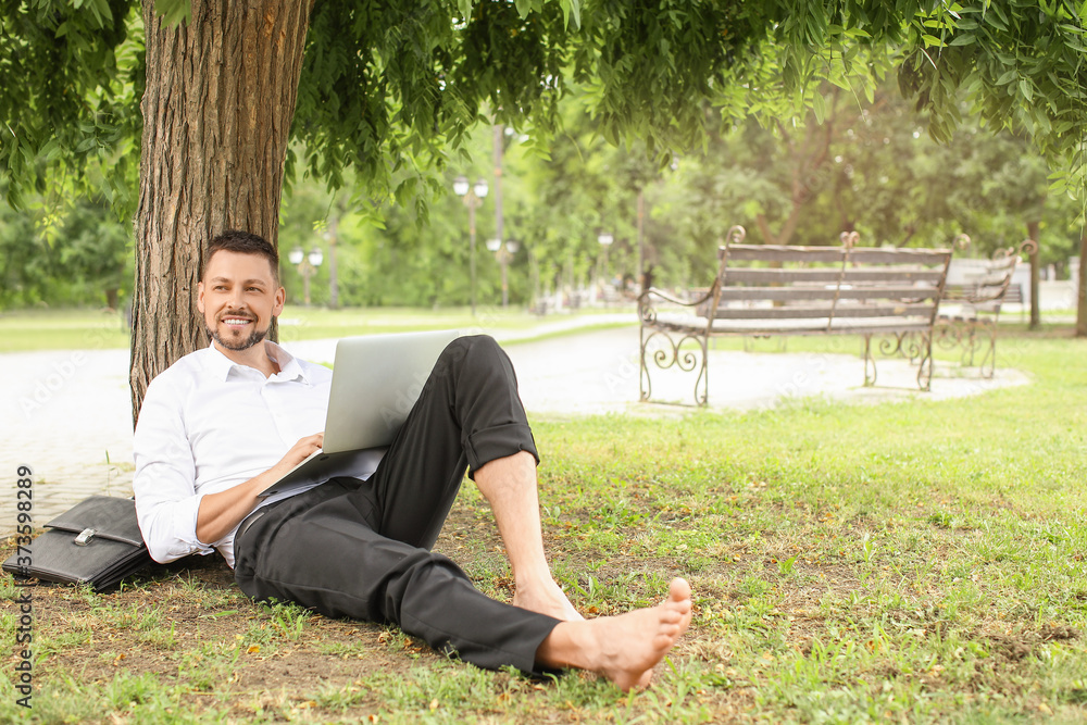 Handsome businessman with laptop relaxing in park