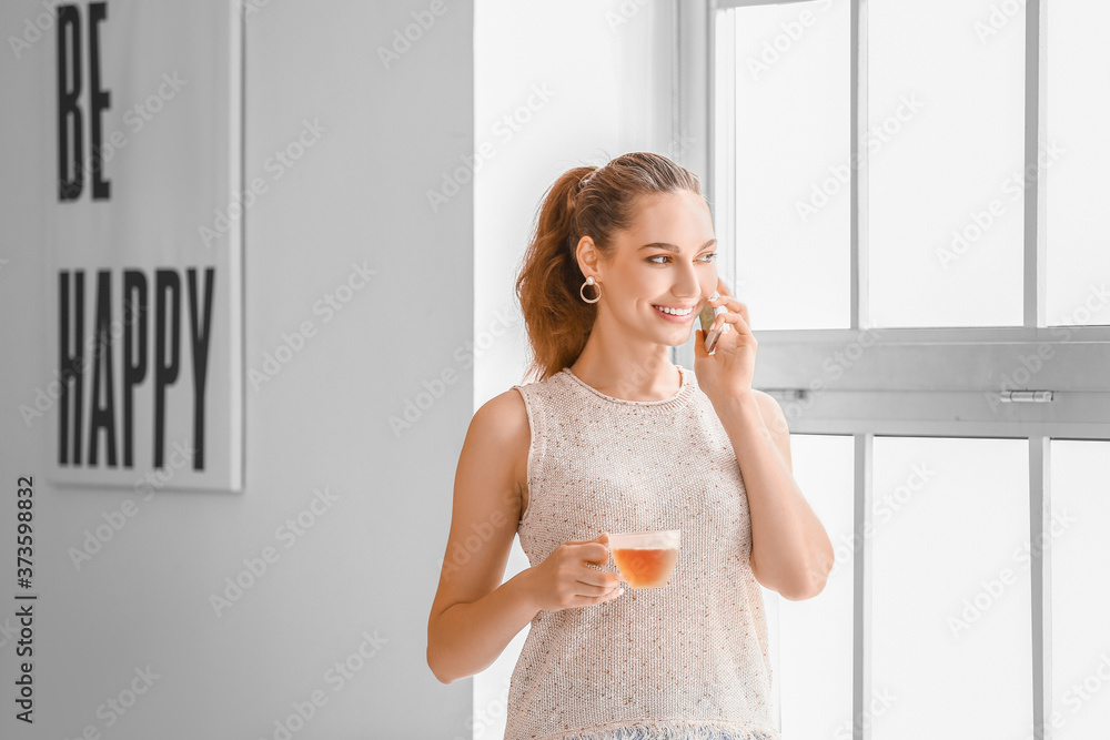 漂亮的年轻女人在家里打电话喝茶