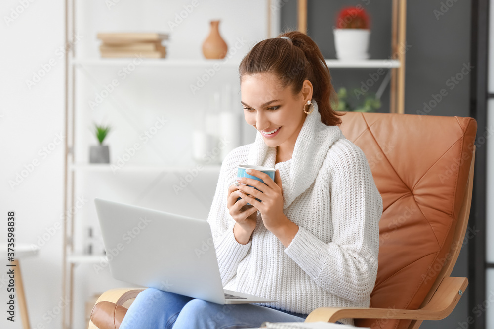 Beautiful young woman with laptop drinking tea at home