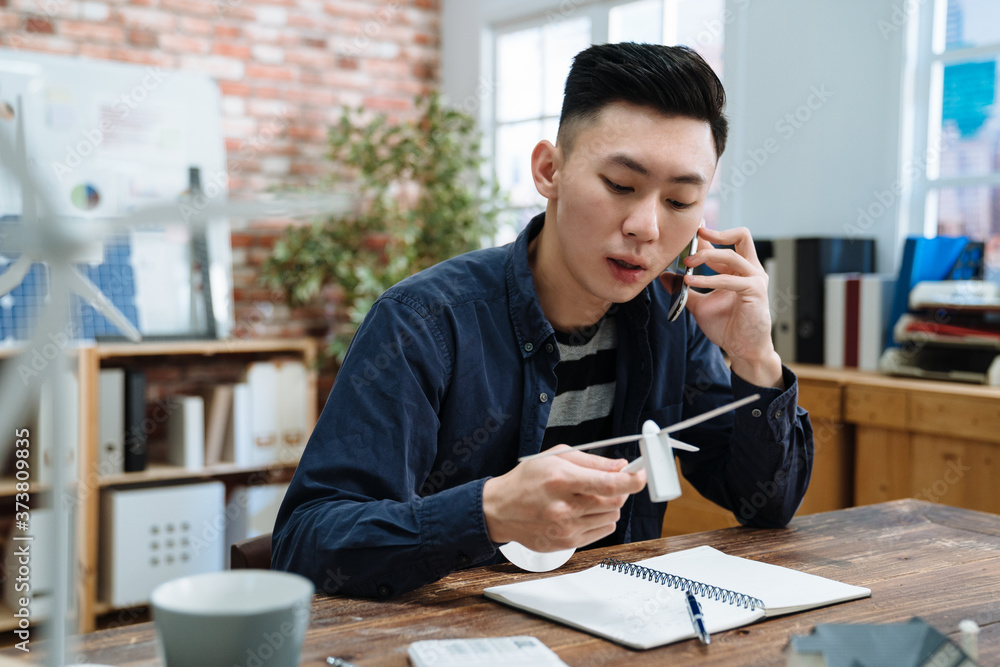 谈判理念。英俊的建筑师手里拿着风车模型，在手机上聊天