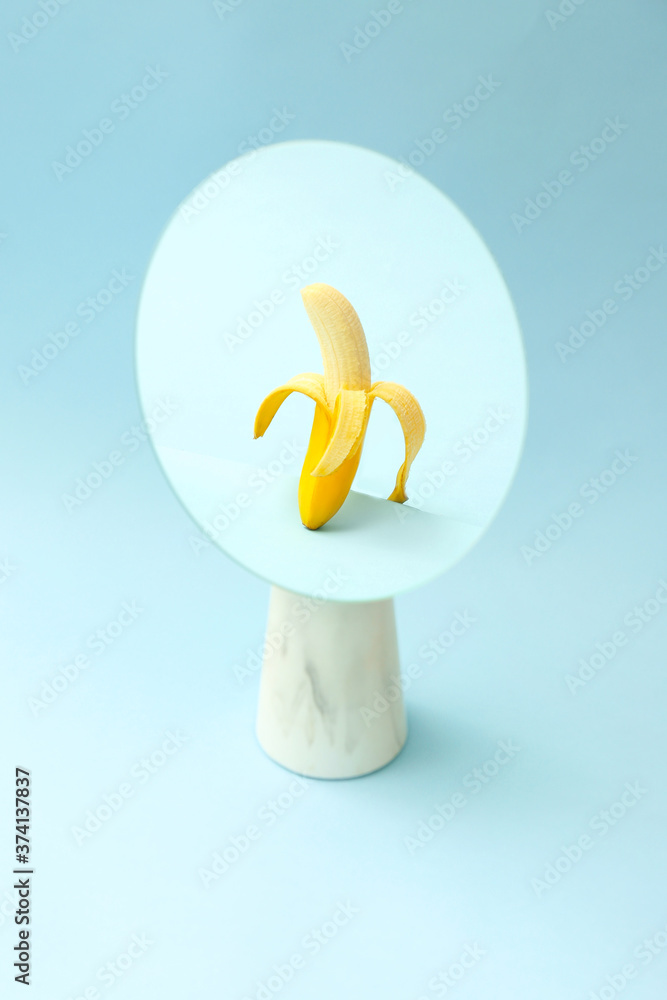 Reflection of banana in mirror on color background