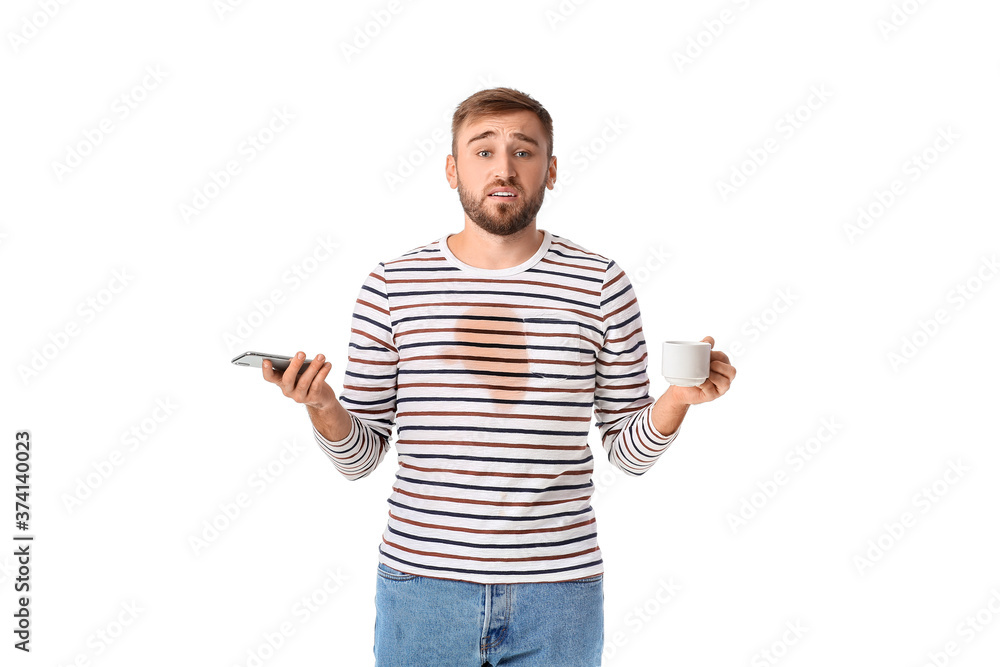 Stressed young man with coffee stains on his t-shirt and mobile phone on white background