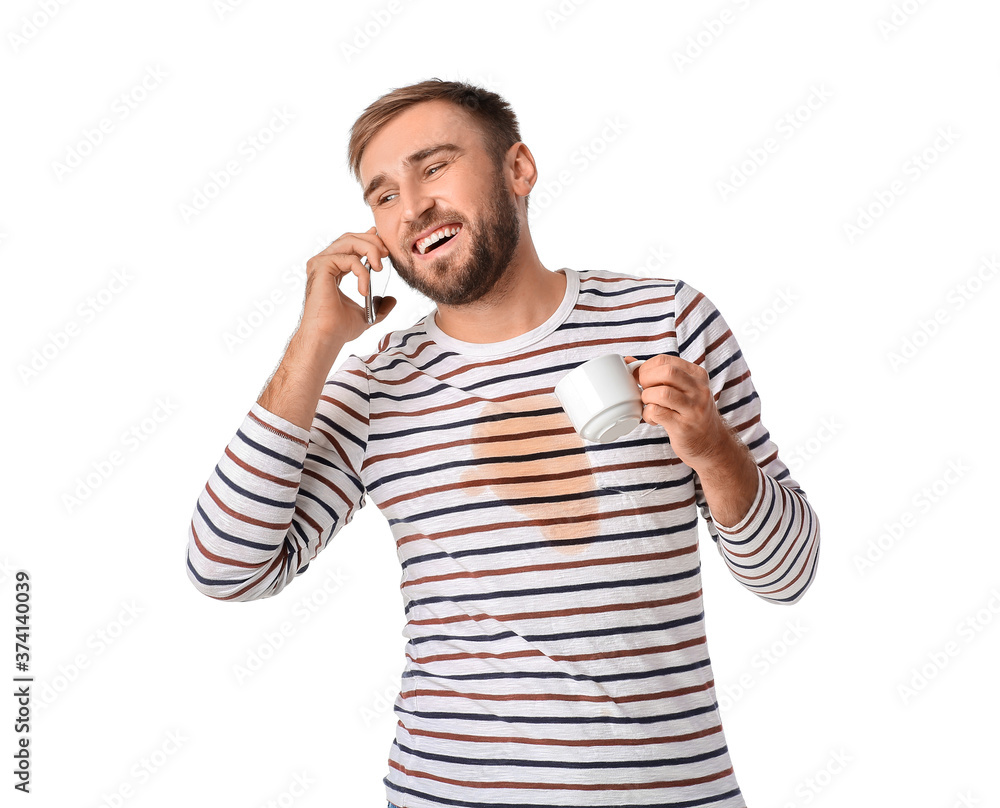 Happy young man with coffee stains on his t-shirt talking by mobile phone on white background