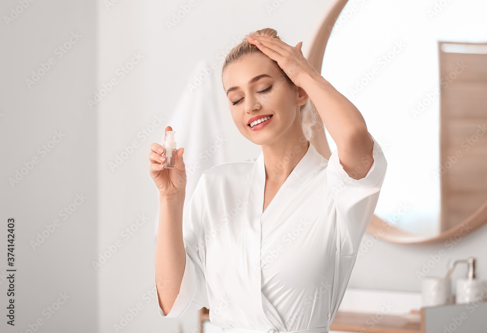 Beautiful young woman applying cosmetic oil in bathroom