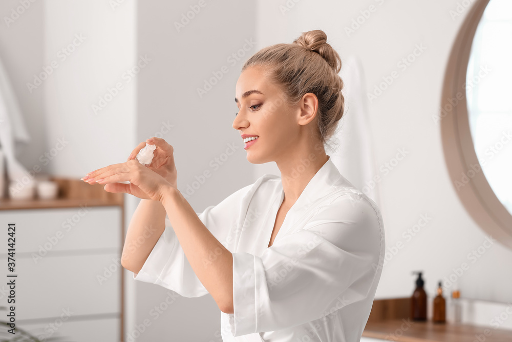 Beautiful young woman applying cosmetic oil in bathroom