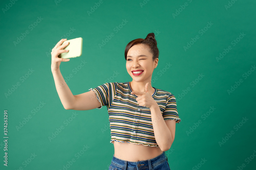 Portrait of smiling young Asian woman holding smartphone in hand shooting selfie over green backgrou