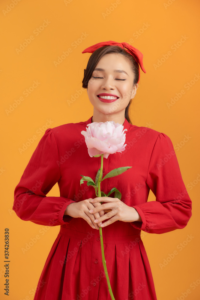 Close up young Asian woman holding peony flower over orange background.