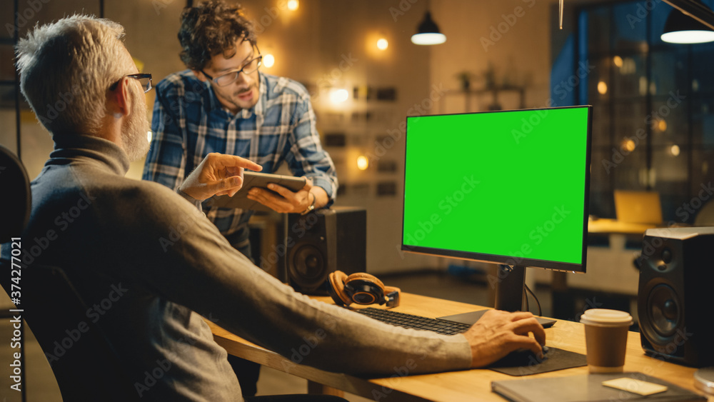 In the Evening Creative Middle Aged Man Works on a Desktop Computer Green Mock-up Screen, Has Conver