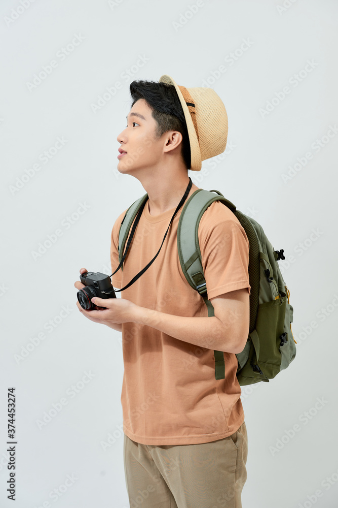 Portrait of cheerful young Asian tourist man holding digital camera and taking photo when standing o