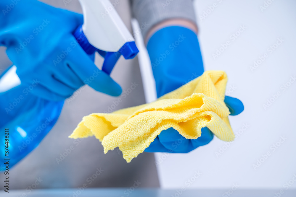 Young woman housekeeper in apron is cleaning, wiping down table surface with blue gloves, wet yellow