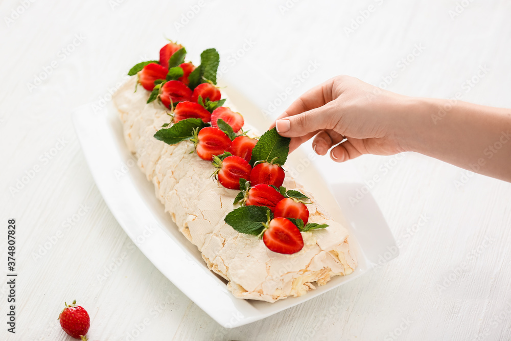 Woman decorating delicious meringue roll with strawberry on plate