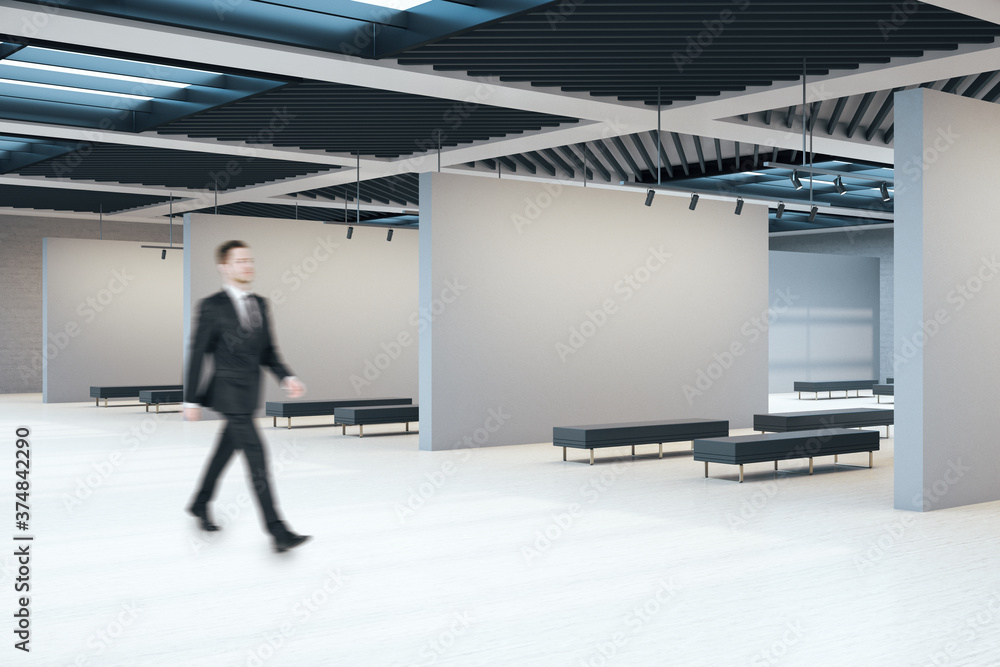 Businessman walking in exhibition hall interior with copyspace on concrete walls