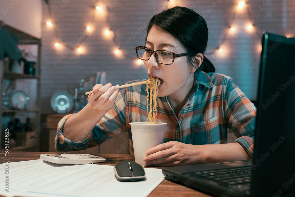 优雅的女商人在餐桌上吃方便面，同时用笔记本电脑加班