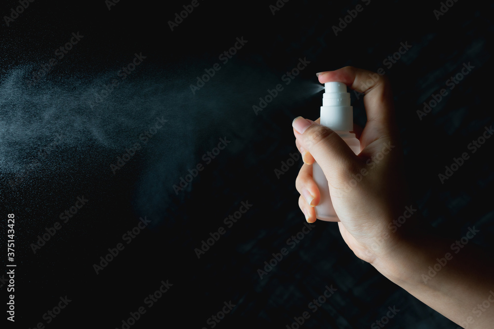 close up woman handing small spray bottle and spraying on dark background