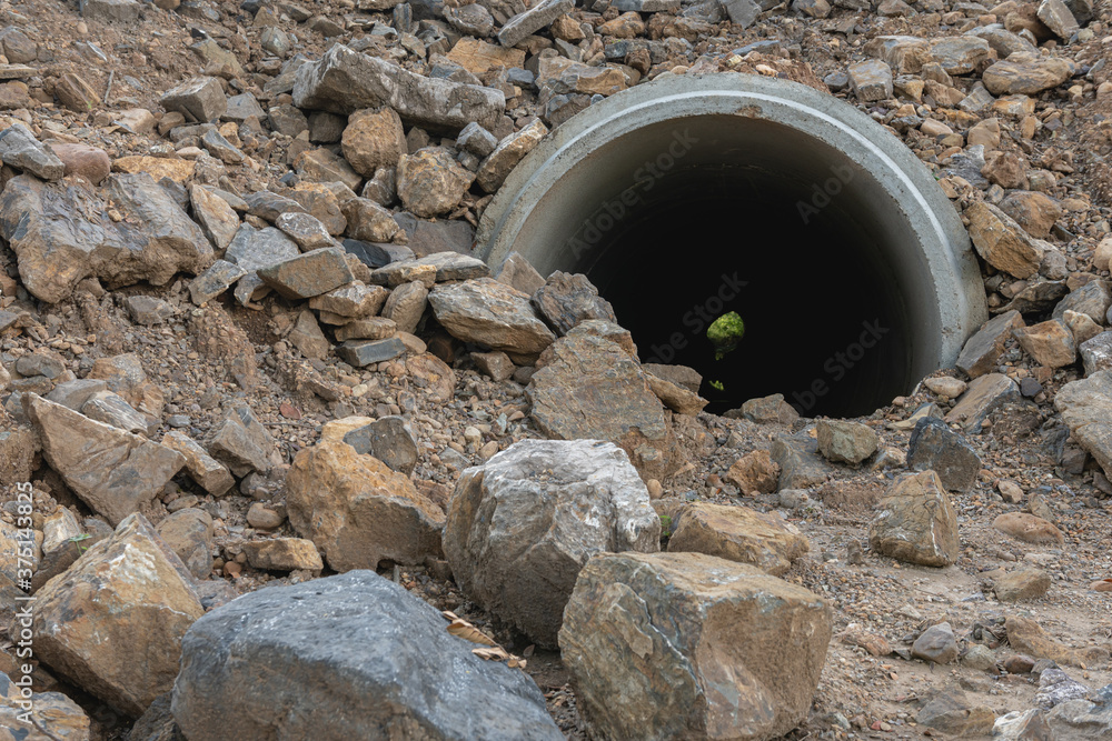 Concrete drain pipe under the ground and rocks