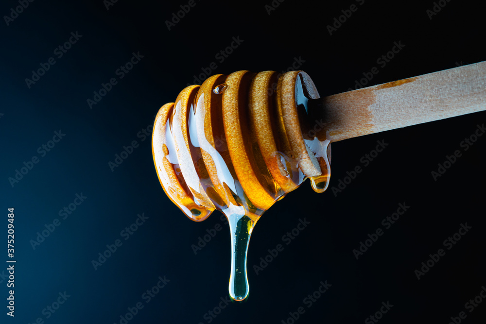 Macro wooden honey dipper and honey on dark background