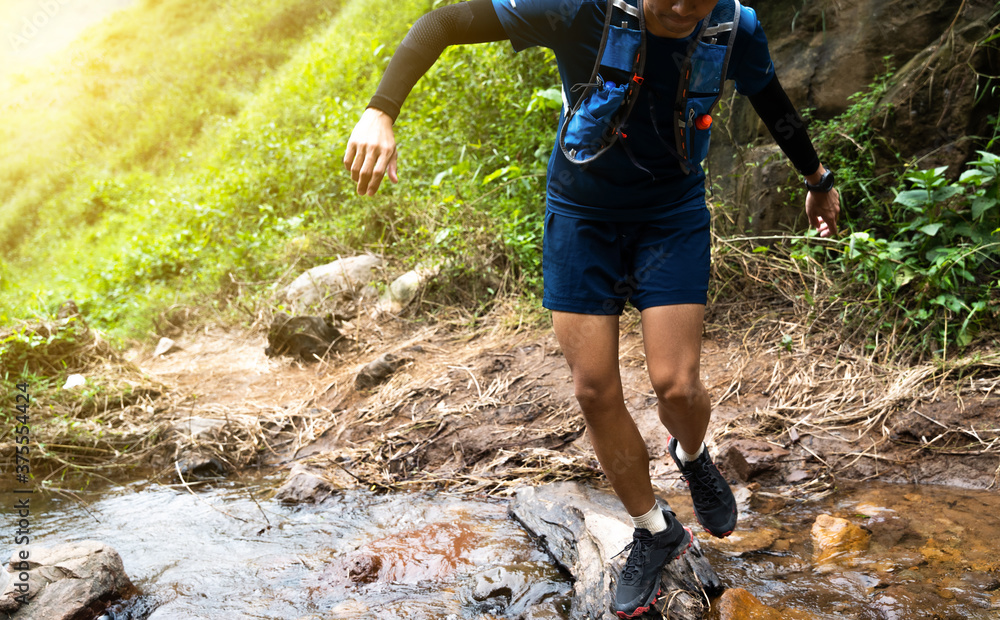 Runner, hes running a trail. In a natural path with a stream