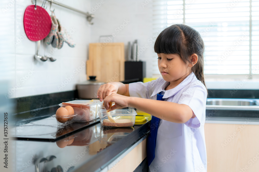 穿着制服的亚洲小学生女孩在早校做午餐盒三明治