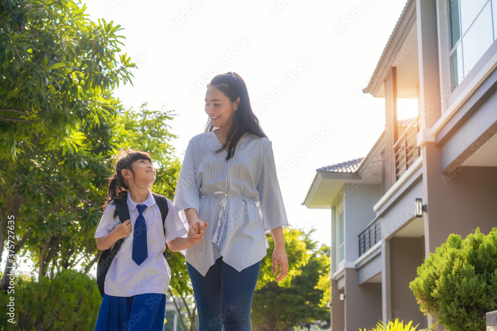 快乐的亚洲母女小学生在上午的学校里步行上学