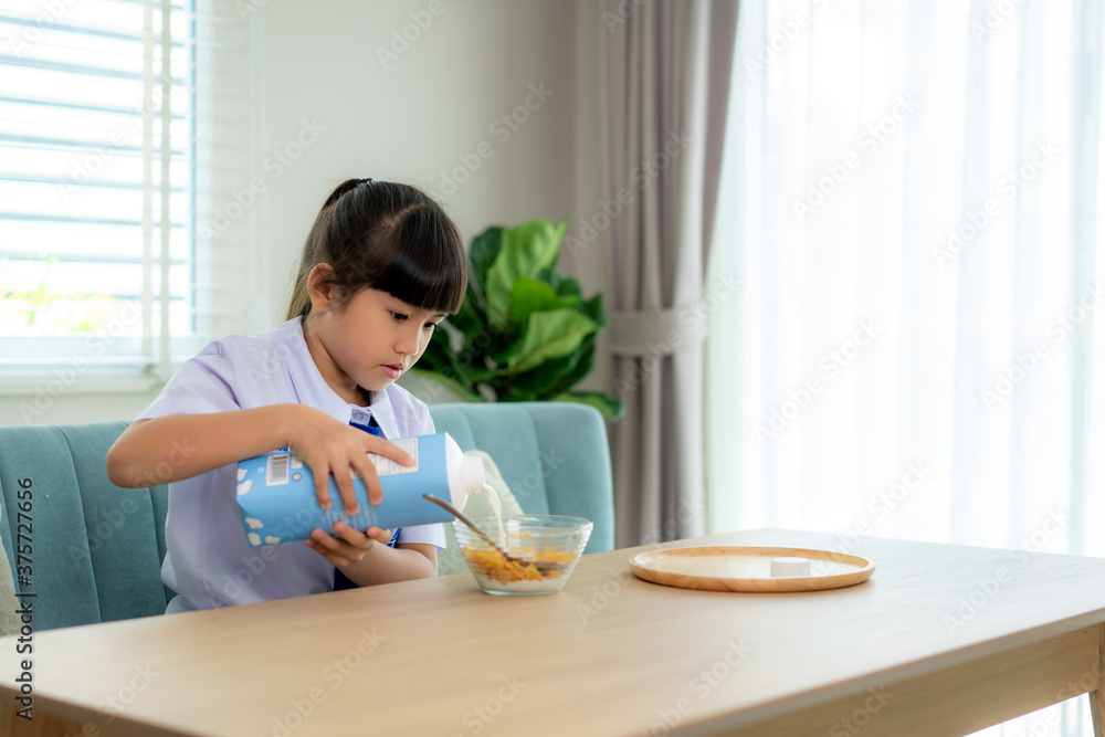 穿着制服的亚洲小学生女孩在早校吃早餐麦片配牛奶