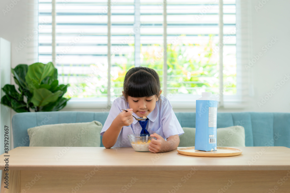 穿着制服的亚洲小学生女孩在早校吃早餐麦片配牛奶