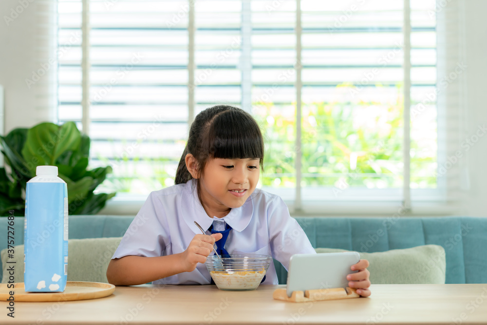 亚洲小学生女孩用牛奶吃早餐麦片，看起来很聪明