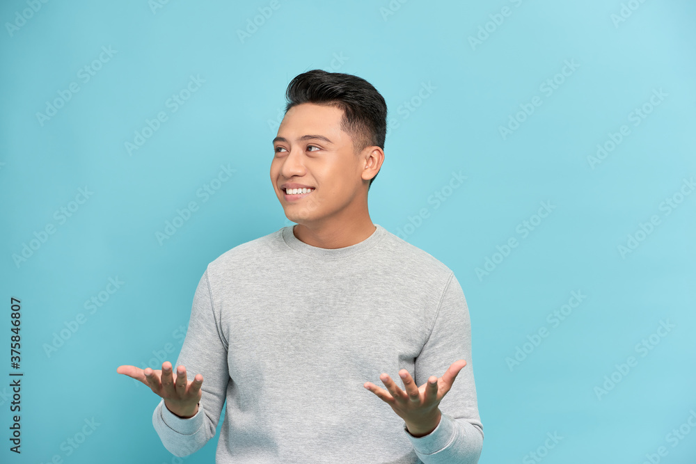 A standing young man raising hands as he saying surprise, isolated on a Blue background.