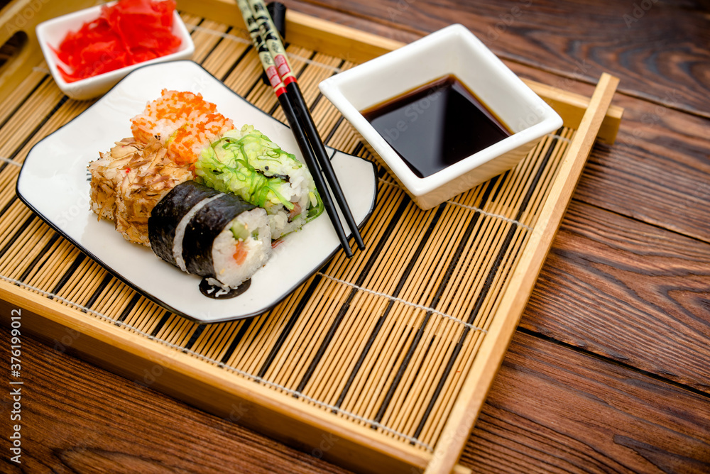 Several sushi on a white plate standing on a brown wooden background
