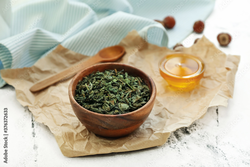 Bowl with dry tea leaves and honey on table