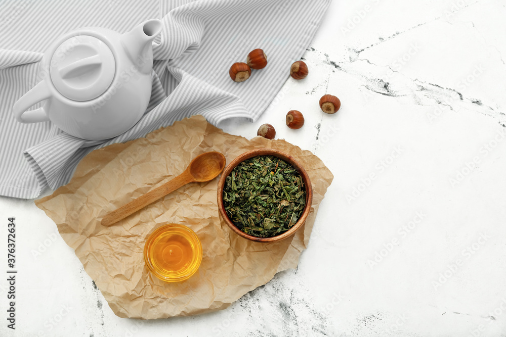 Bowl with dry tea leaves, teapot and honey on table