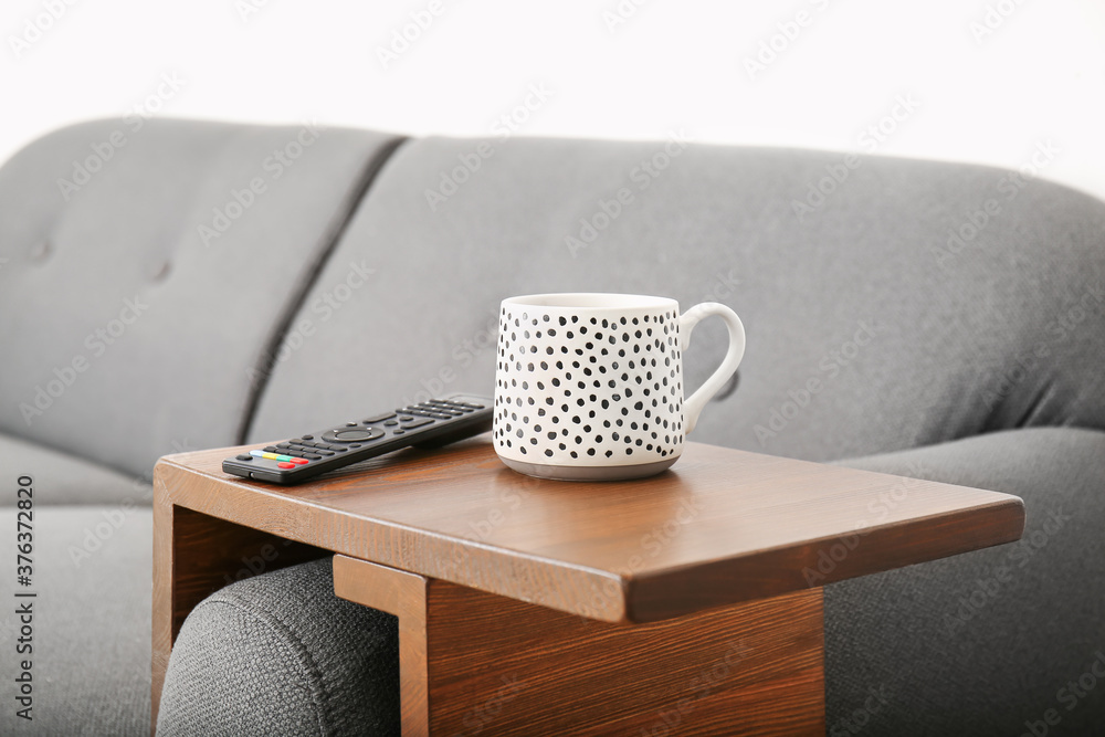 Cup of tea with remote control on armrest table in room