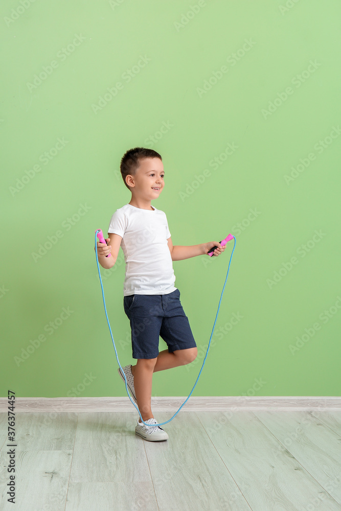 Cute little boy jumping rope near color wall