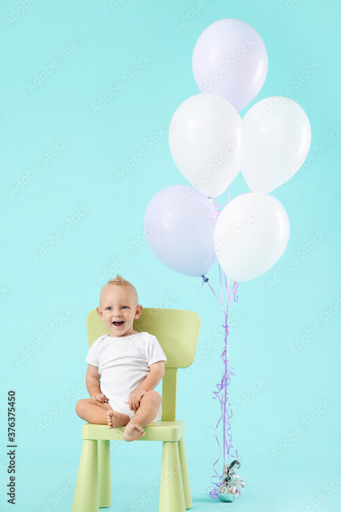 Portrait of cute little baby with air balloons on color background