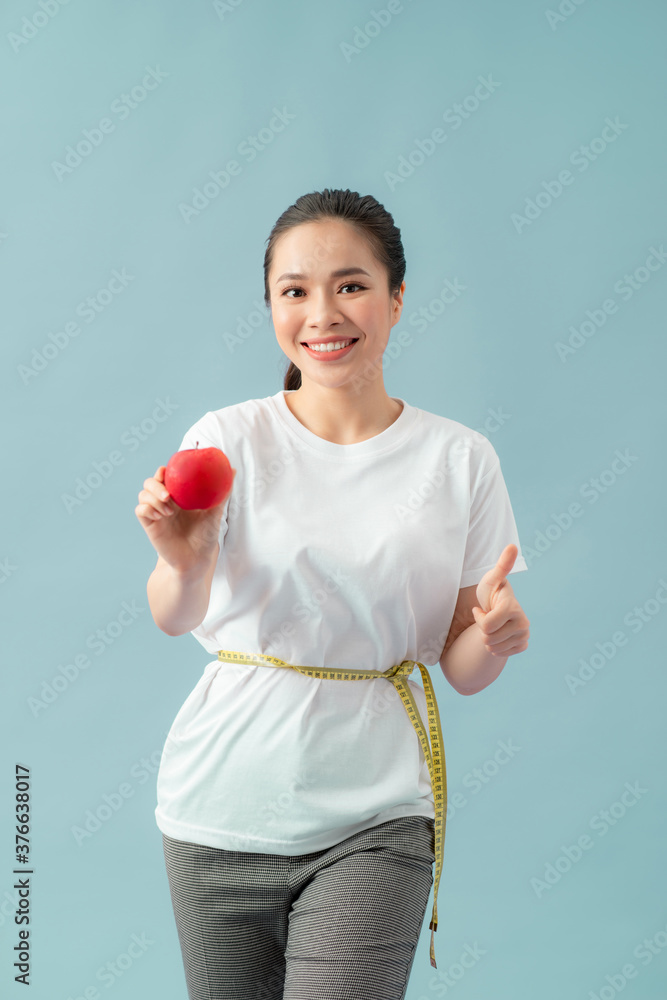 漂亮的运动型女人用卷尺吃苹果果，竖起大拇指，开心地笑着。