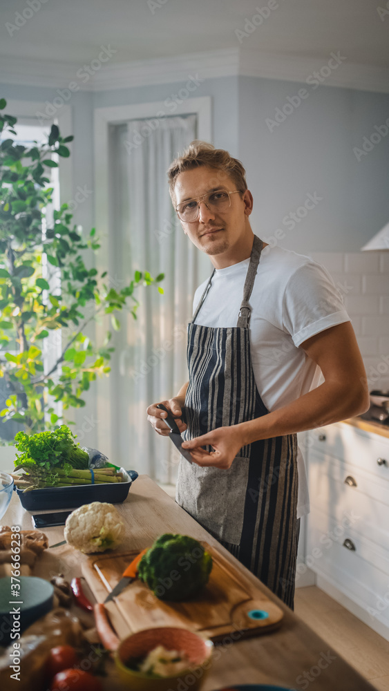 穿着白衬衫和围裙的英俊男人在现代阳光厨房里做健康的有机沙拉餐