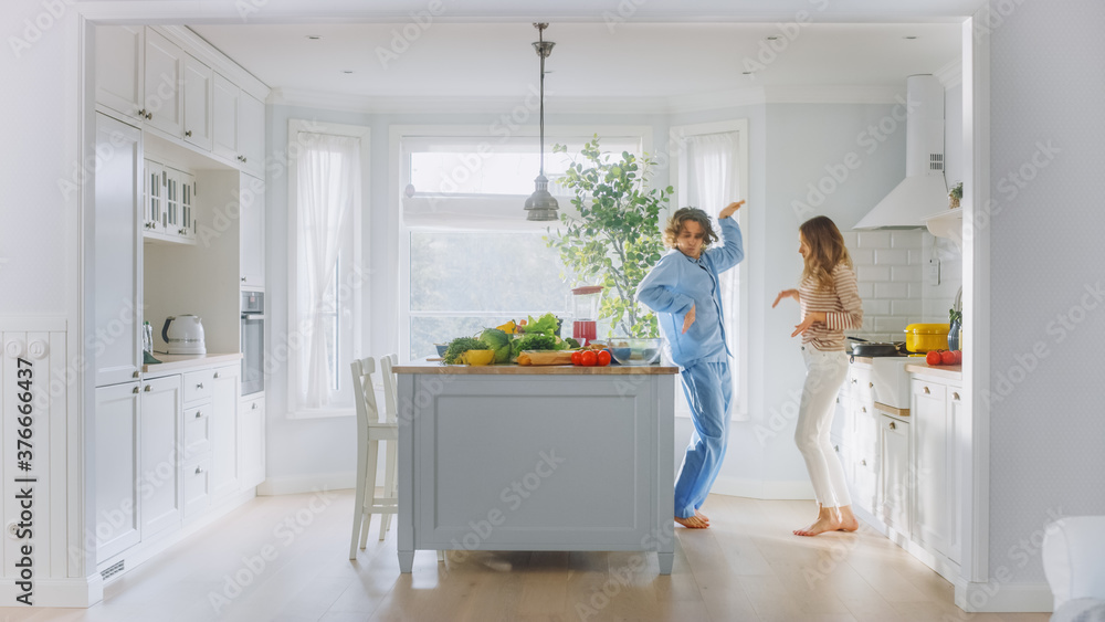 Handsome Young Man in Blue Pajamas and Beautiful Girl in Striped Jumper are Dancing in the Kitchen. 