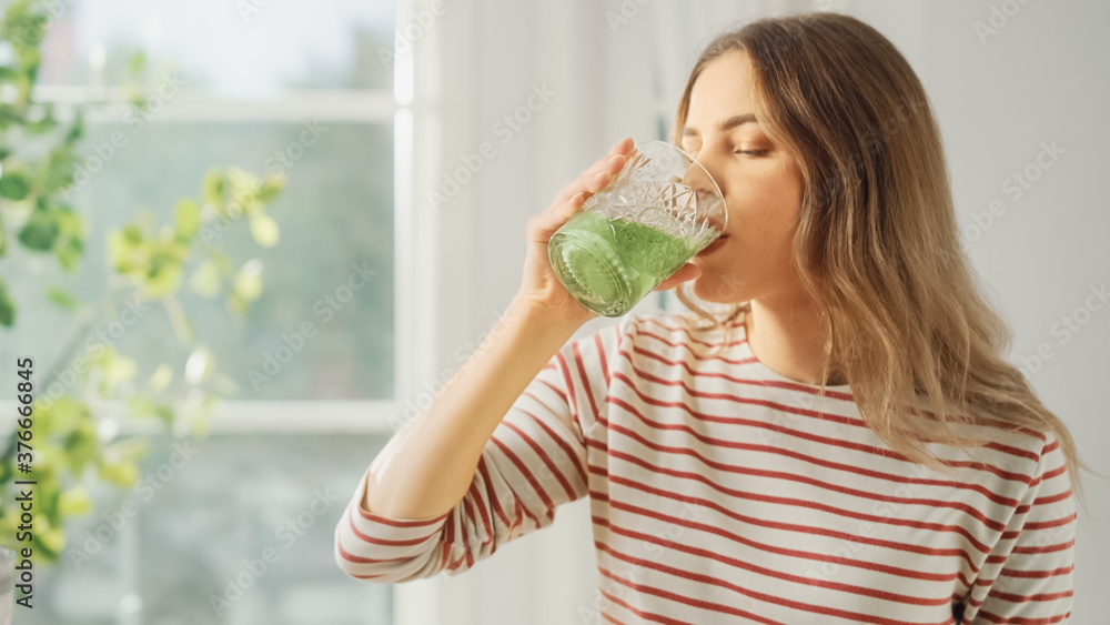 Beautiful Young Female Drinking a Healthy Green Smoothie from a Glass. Authentic Stylish Kitchen wit