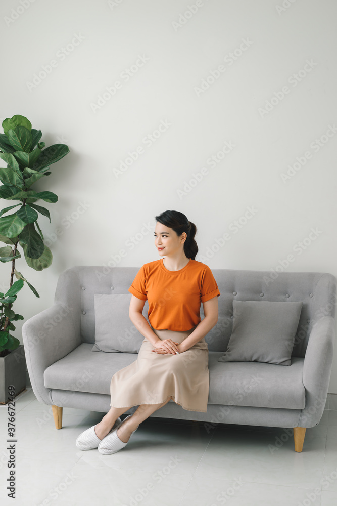 Portrait of smiling young housewife sitting on couch in living room