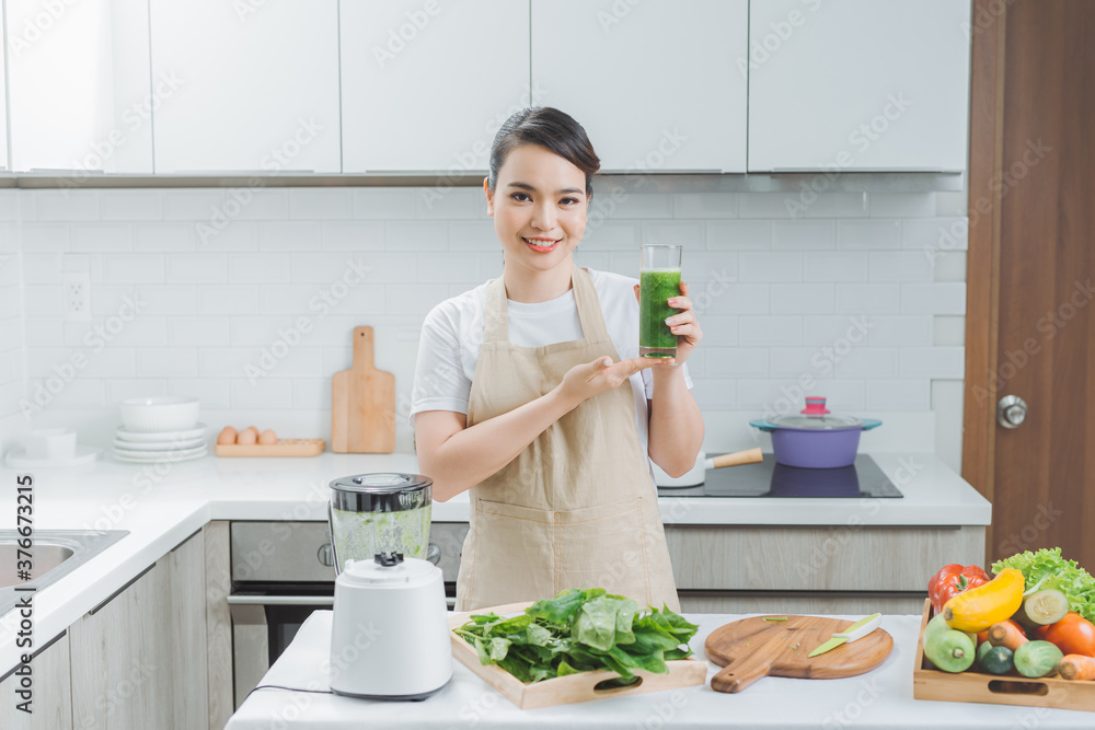 young asian woman drinking green fresh vegetable juice or smoothie from glass at home.